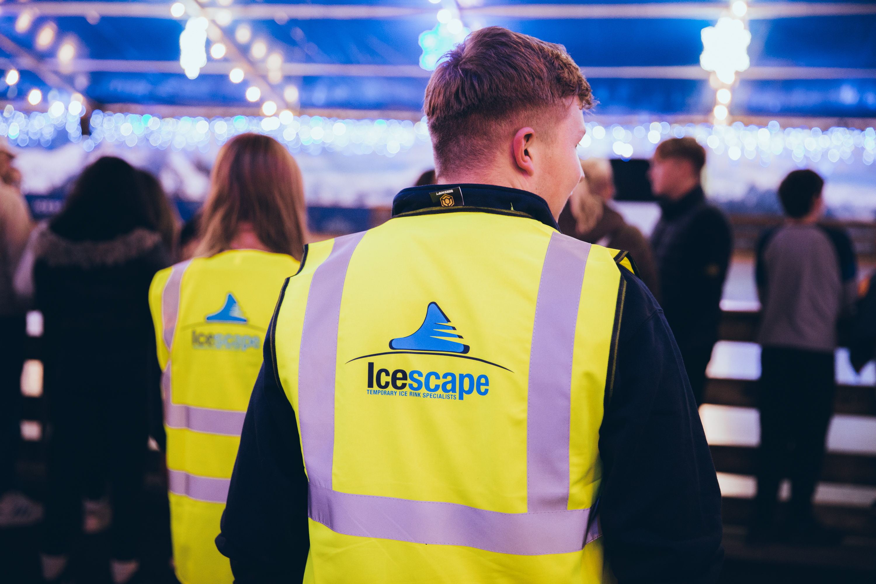 Two Icescape staff members in yellow hi-vis vests working at one of their temporary real ice rinks. 
