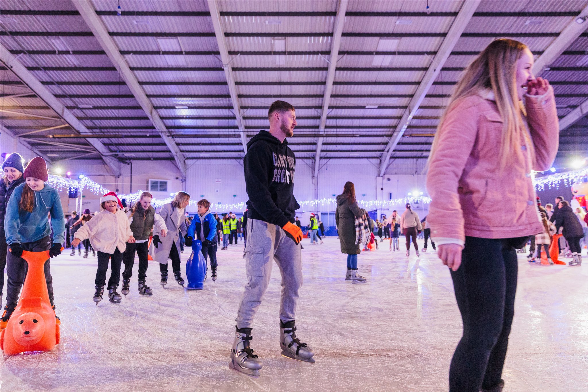 Ice skaters enjoying the ice at Icescape Westpoint, Exeter. A large ice rink, with skaters of all ages and skate aids on the ice. 
