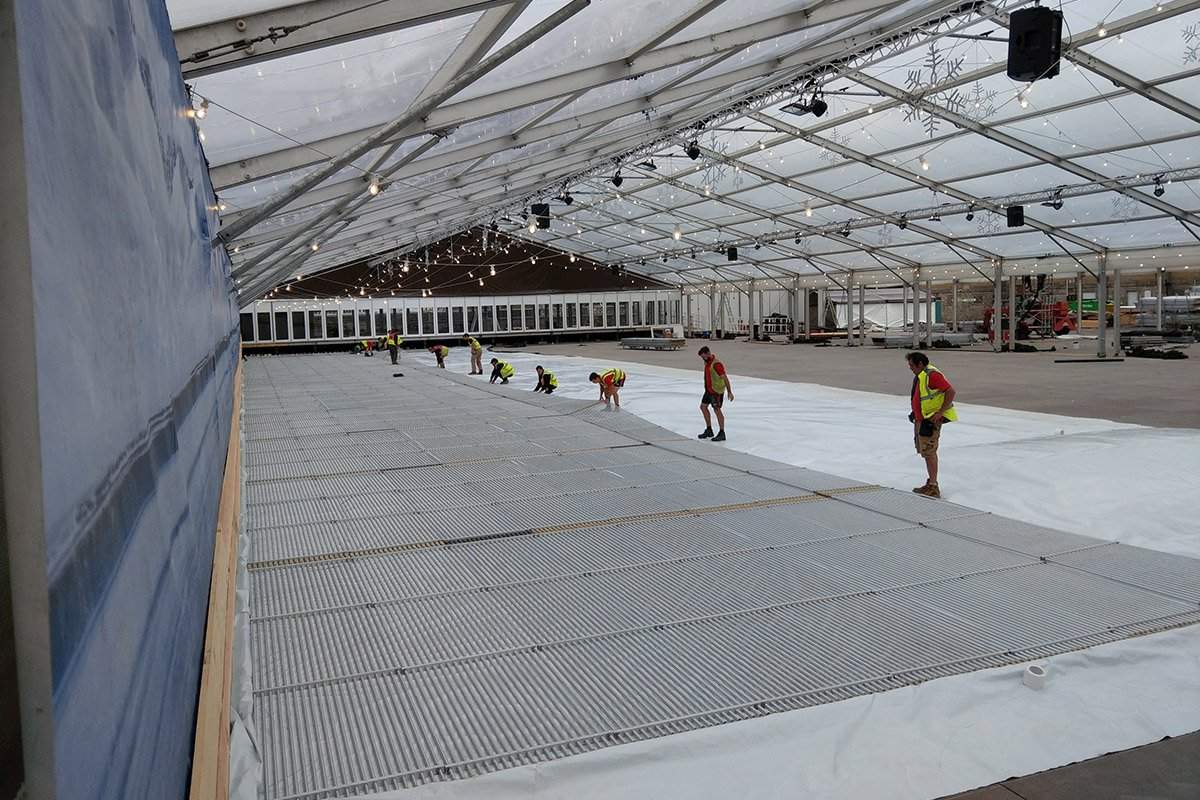 Icescape Ltd rink system. Inside a large marquee structure, workers are laying out the beginning process of the ice rink with aluminum piping