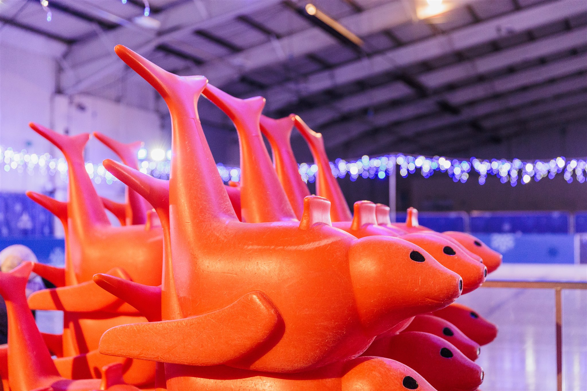 A group of orange skate aids stacked at a temporary real ice rink. 