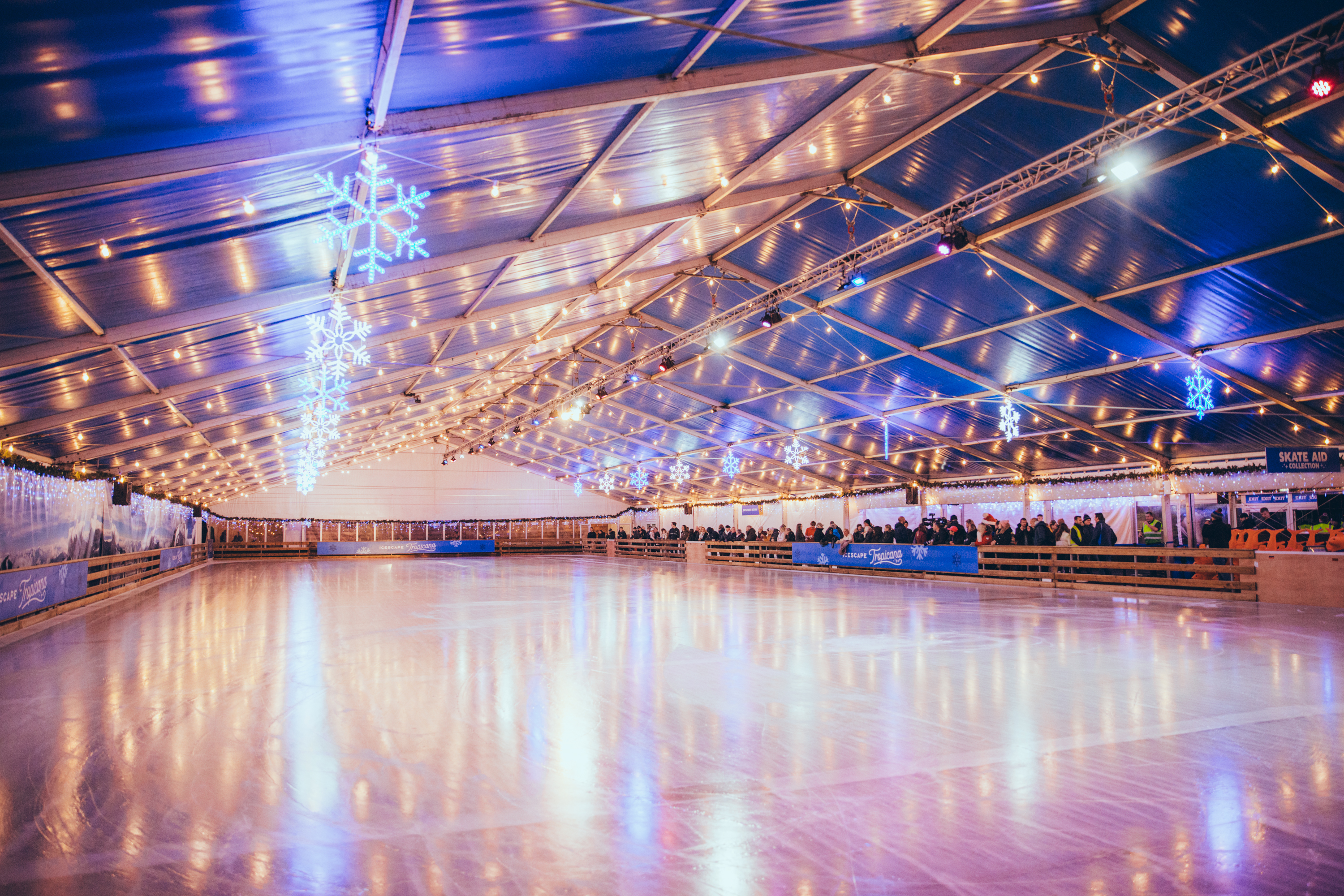 A huge winter real ice temporary rink. Its empty under twinkly lights and covered by a large blue marquee structure. 