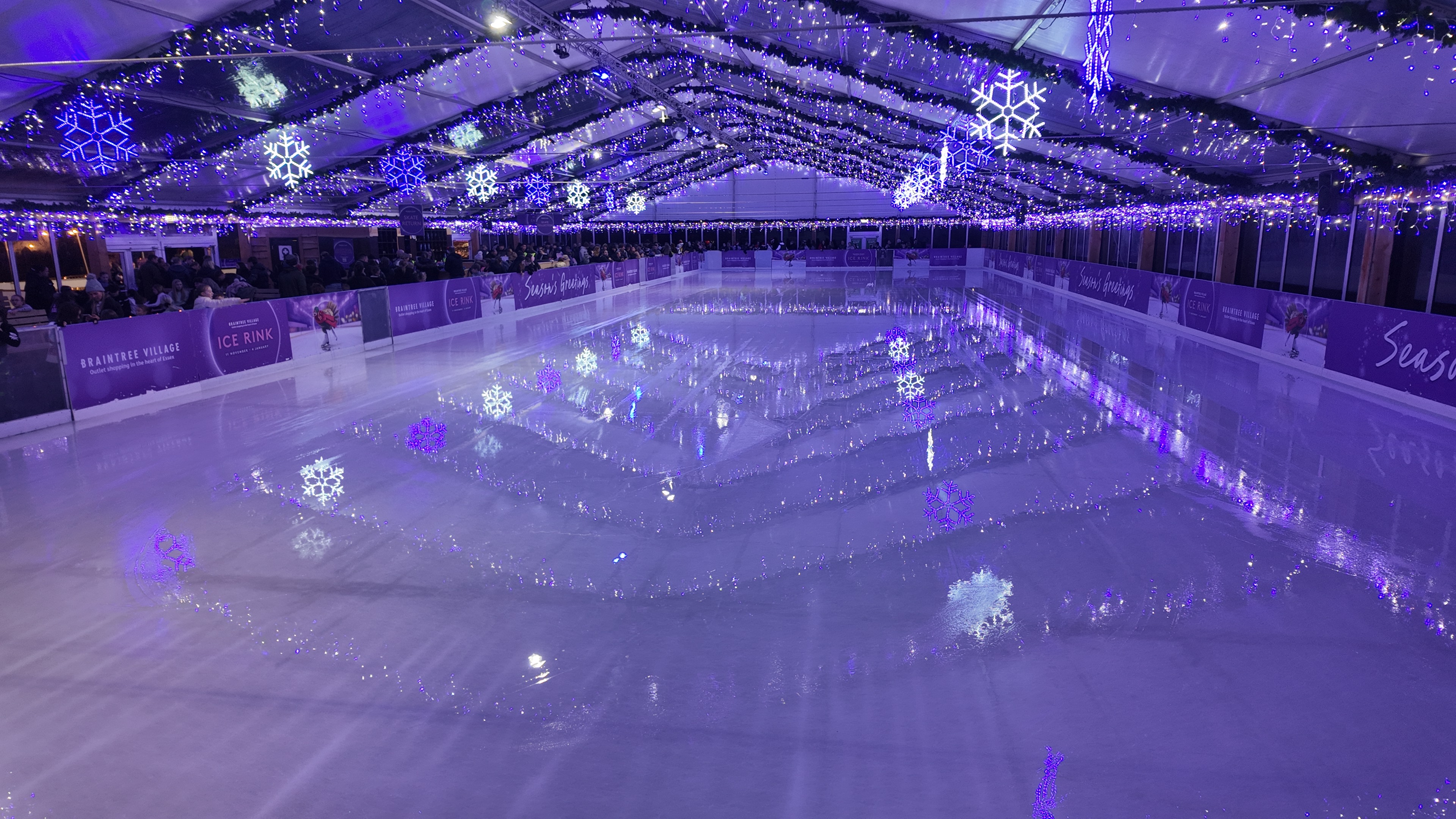 An emptywinter ice rink after a wet ice resurface. The hanging icicles in the marquee roof can also be seen reflecting in the ice. 