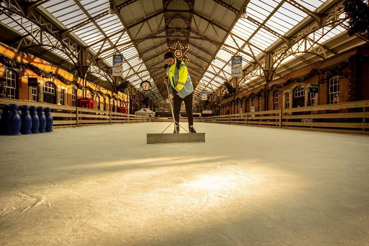 staff member on the ice at Dover winter ice rink, maintaining the ice with manual metal scraper