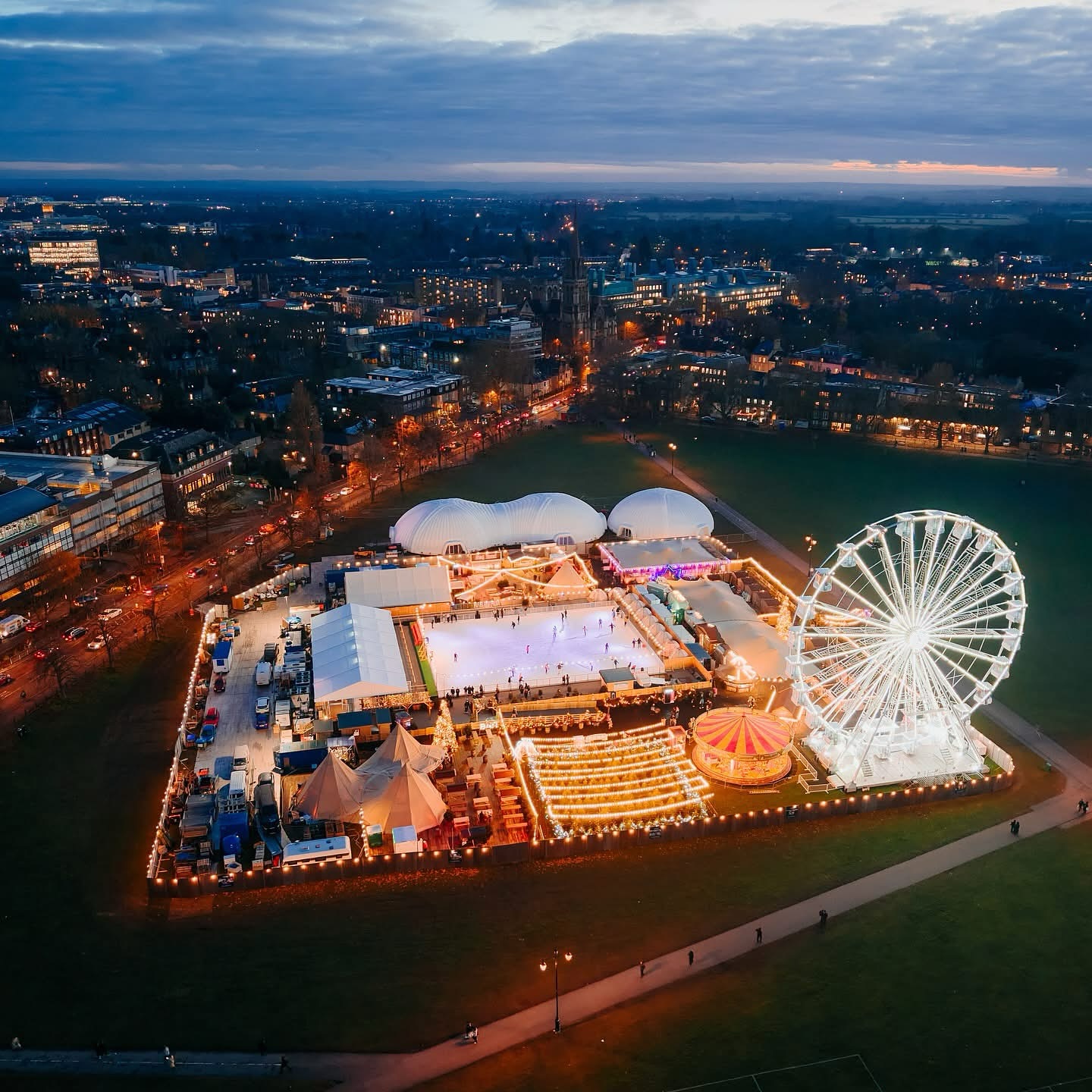 Aerial Shot of the ice rink at Cambridge 2025. The event in a central park has rides, an observation wheel, bars and markets surrounding the ice rink. 