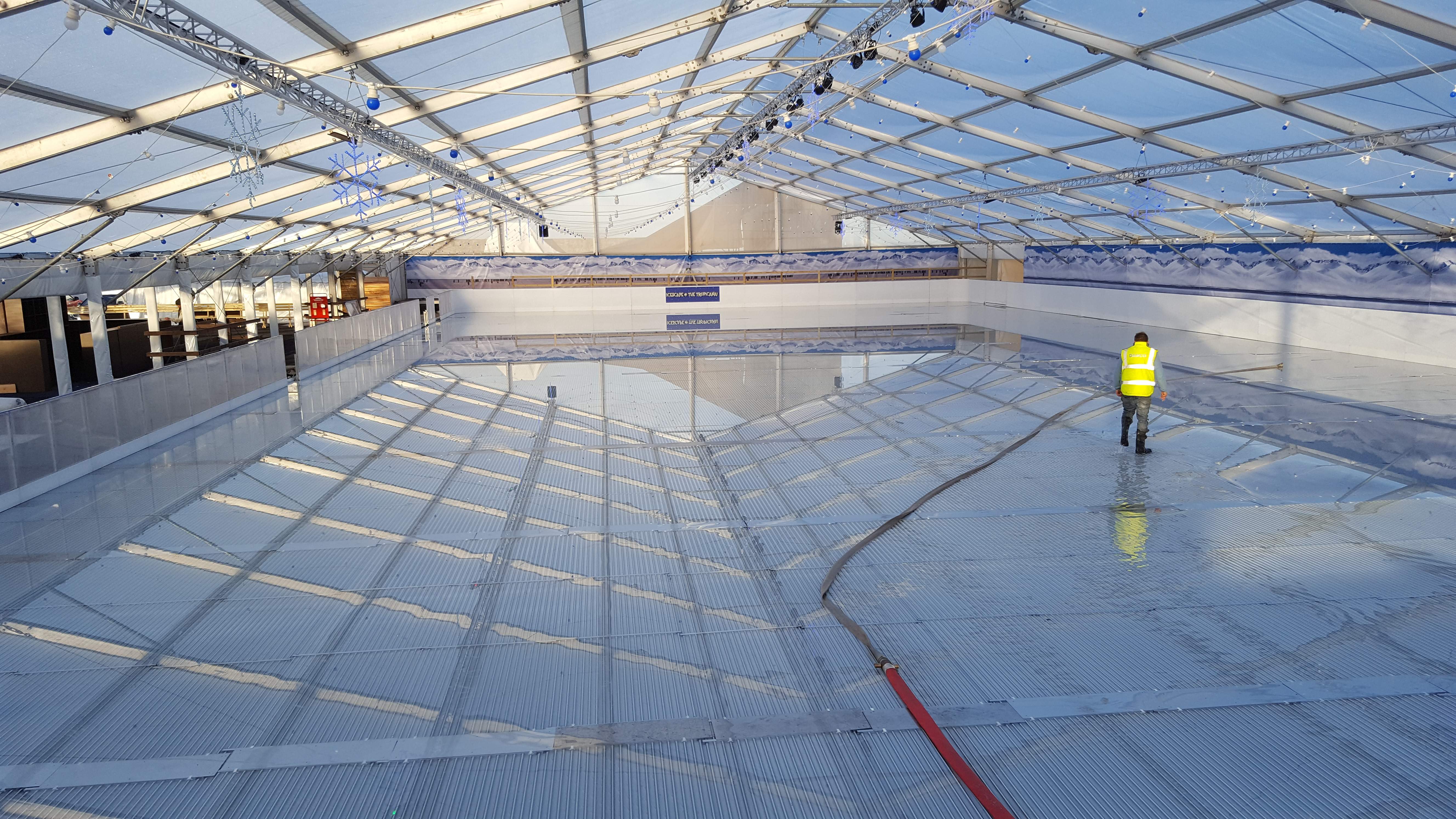An Icescape temporary real ice rink being flooded with water as the worker builds the water levels to create ice. Icescape's aluminum piping system is on display on marquee floor. 