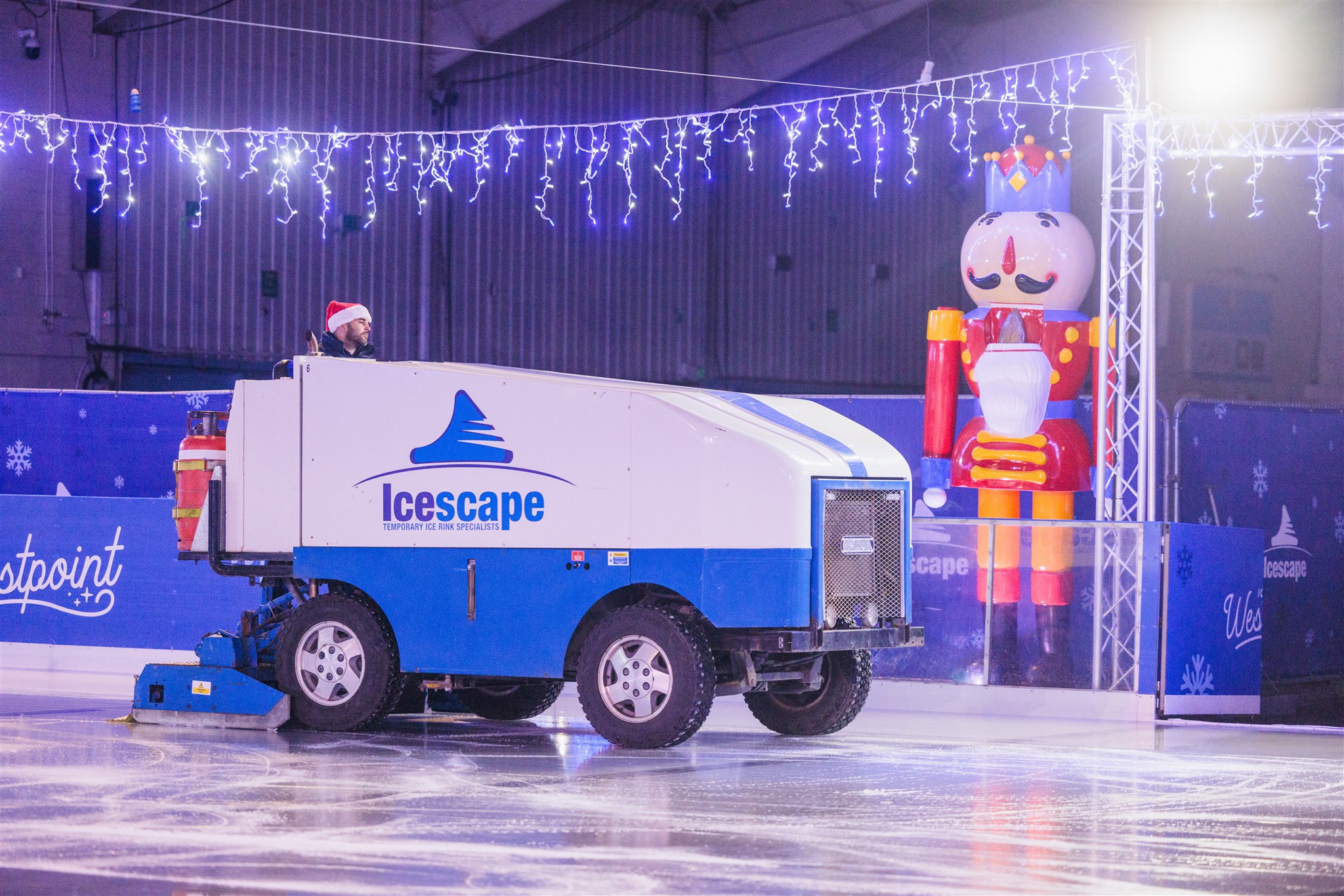 An Olympia ice resurfacer maintaining the ice at a winter ice rink inside Westpoint Arena, Exeter. Icescape branding is on the machine and in the background is a large nutcracker prop. 